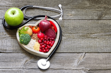 Stethoscope on the table with heart plate filled with fruits and vegetables.