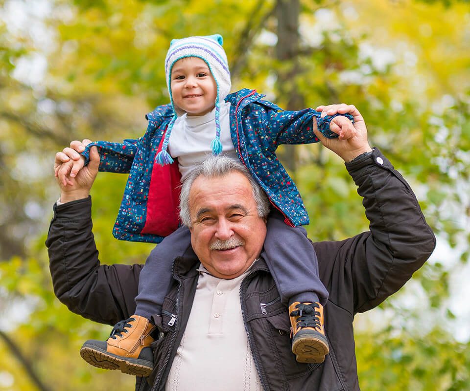 grandfather holding grandson on shoulders outdoors