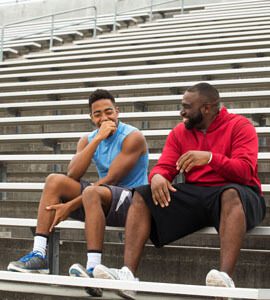 Teen track and field athlete and his coach talk on the bleachers after practice